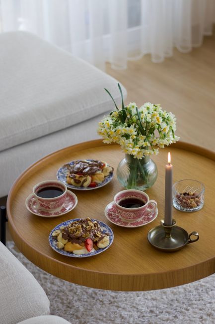 Cozy tea setting with elegant cups, pastries, and a lit candle on a wooden table.