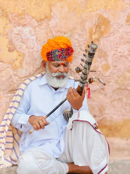 An old man with a turban and a long beard playing a flute