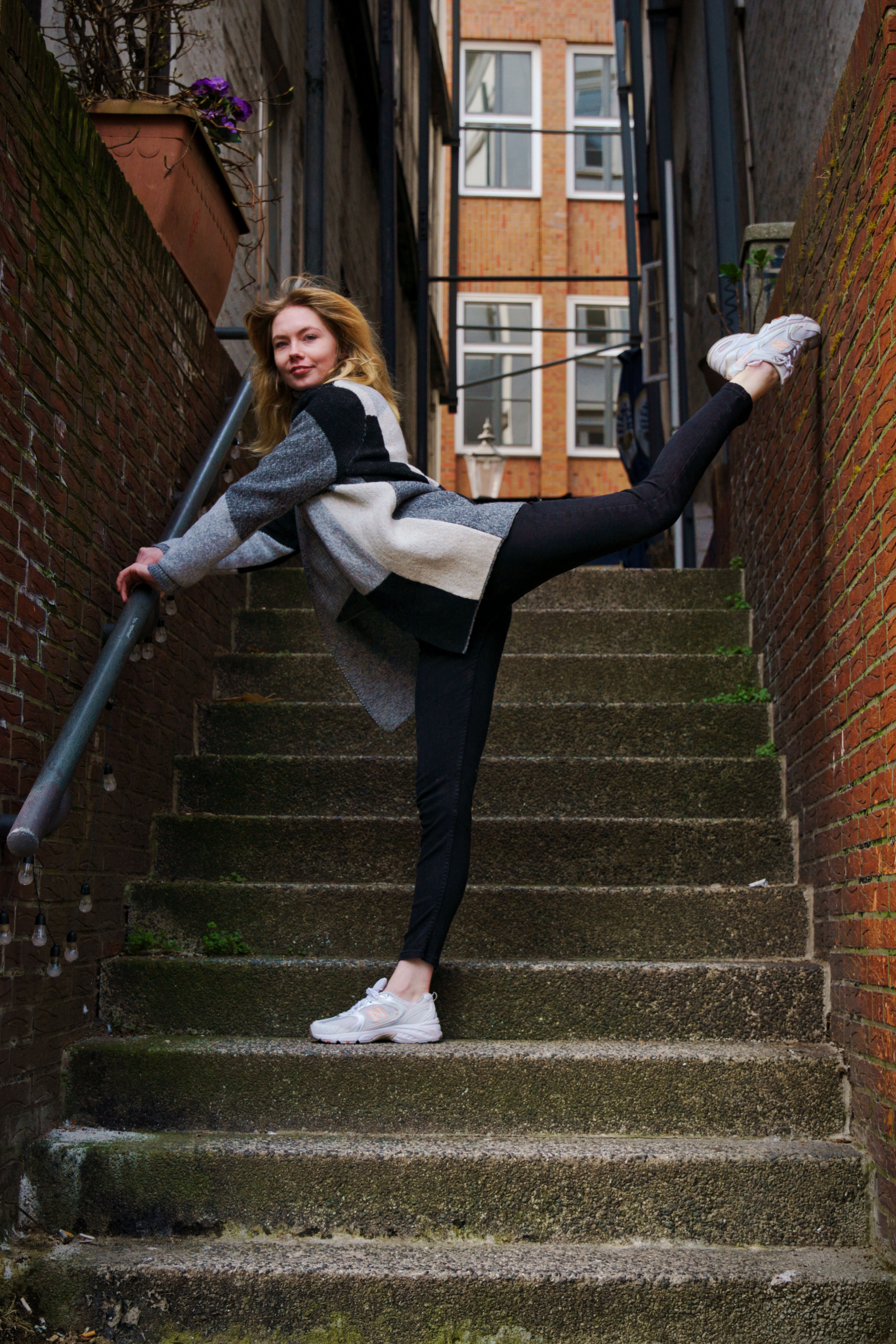 Young woman stretching on a narrow staircase in urban Hamburg, Germany, showcasing fashion and flexibility.