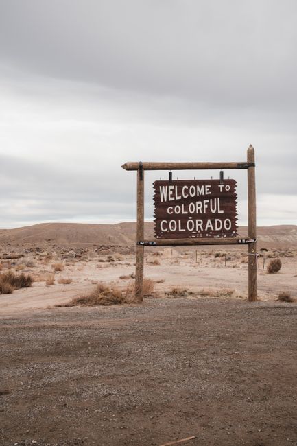 Desert scene with a Welcome to Colorful Colorado sign, overcast sky.