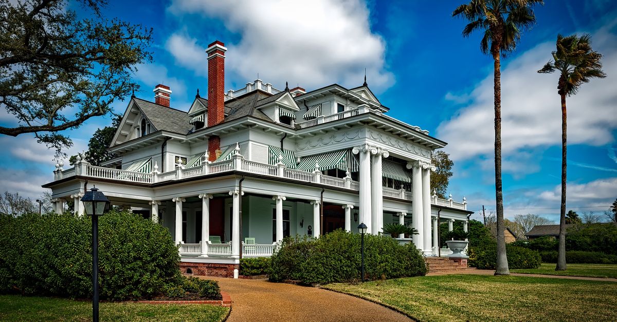 Beautiful white mansion with pillars and palm trees under a bright blue sky.
