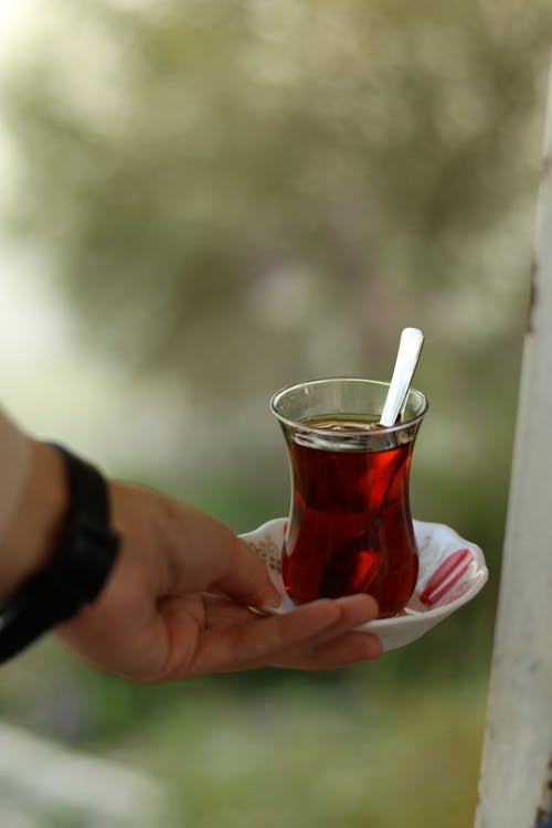 A person holding a cup of tea with a spoon