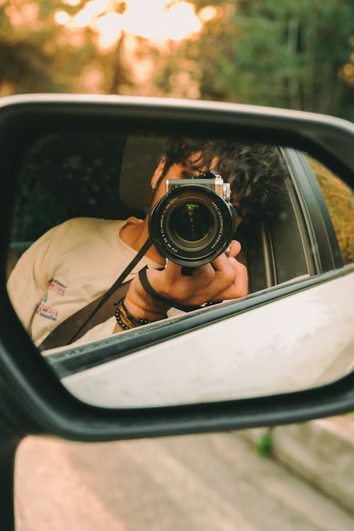 A man taking a photo in the side mirror of a car