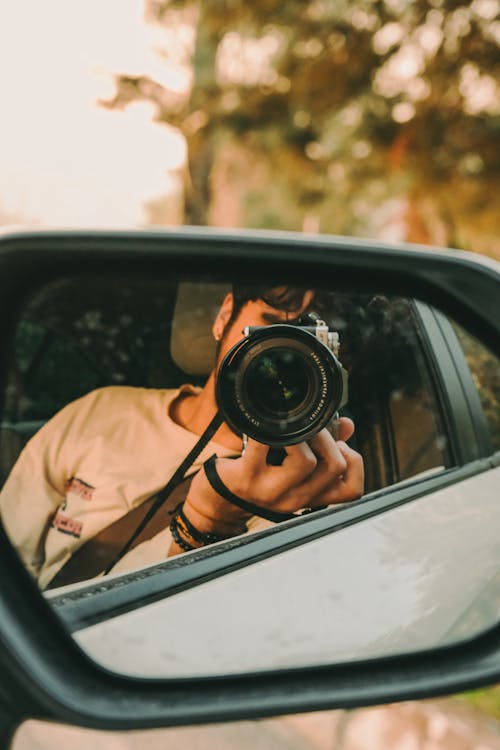 A man taking a photo in the side mirror of a car