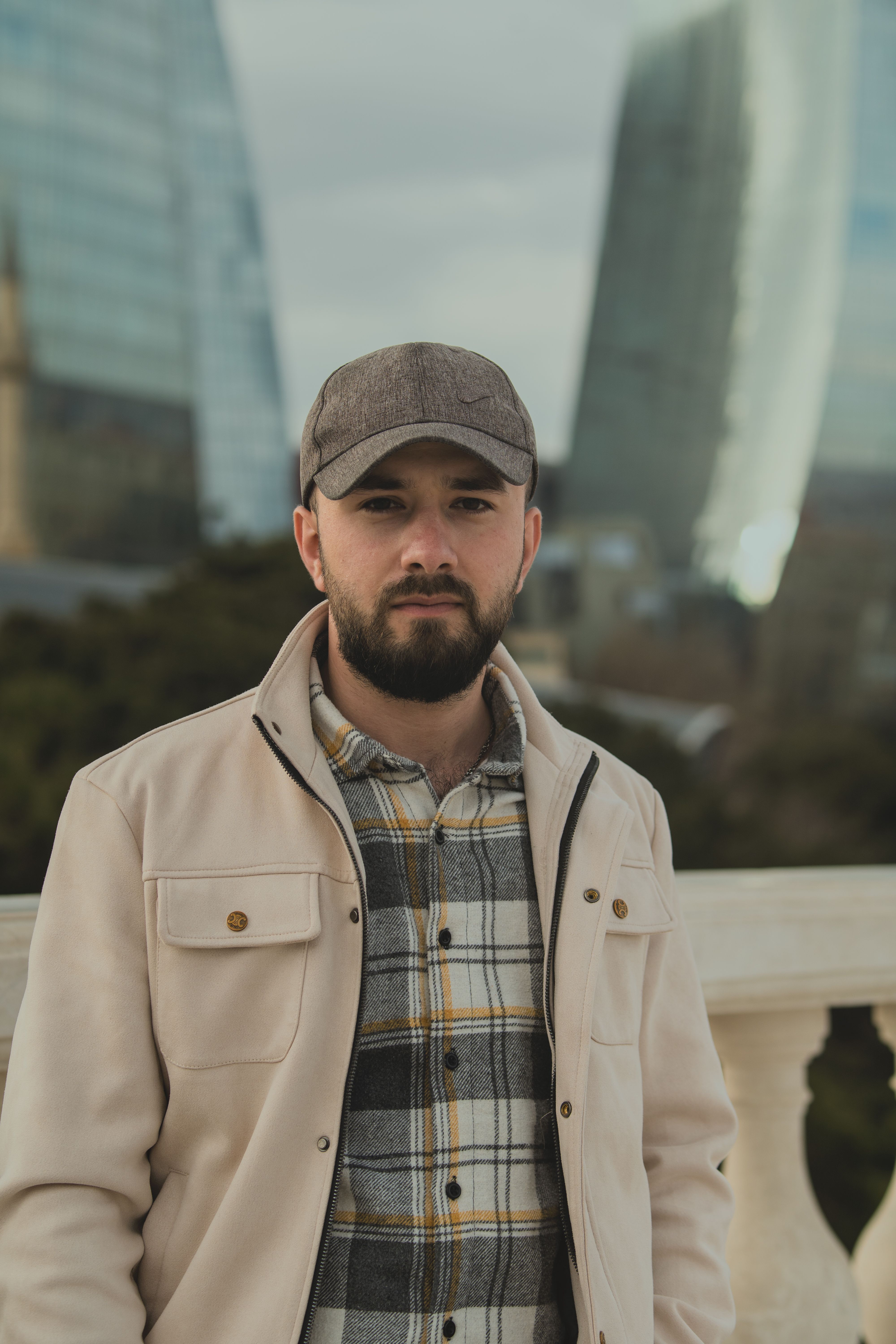 Man with beard and cap in urban setting with skyscrapers.