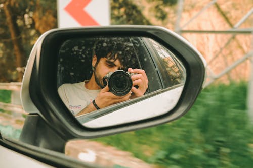 A man taking a photo in the side mirror of a car
