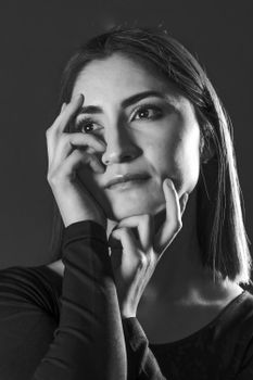 A dramatic black and white portrait of a woman posed thoughtfully, highlighting shadows and expression.