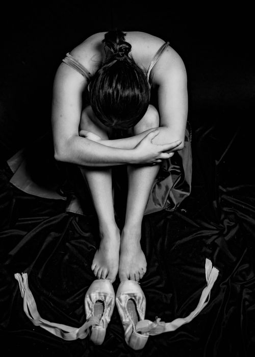Free A ballerina sits barefoot, conveying emotions, with ballet shoes in focus. Stock Photo