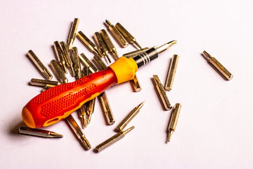 A red screwdriver and a pile of screws on a white background