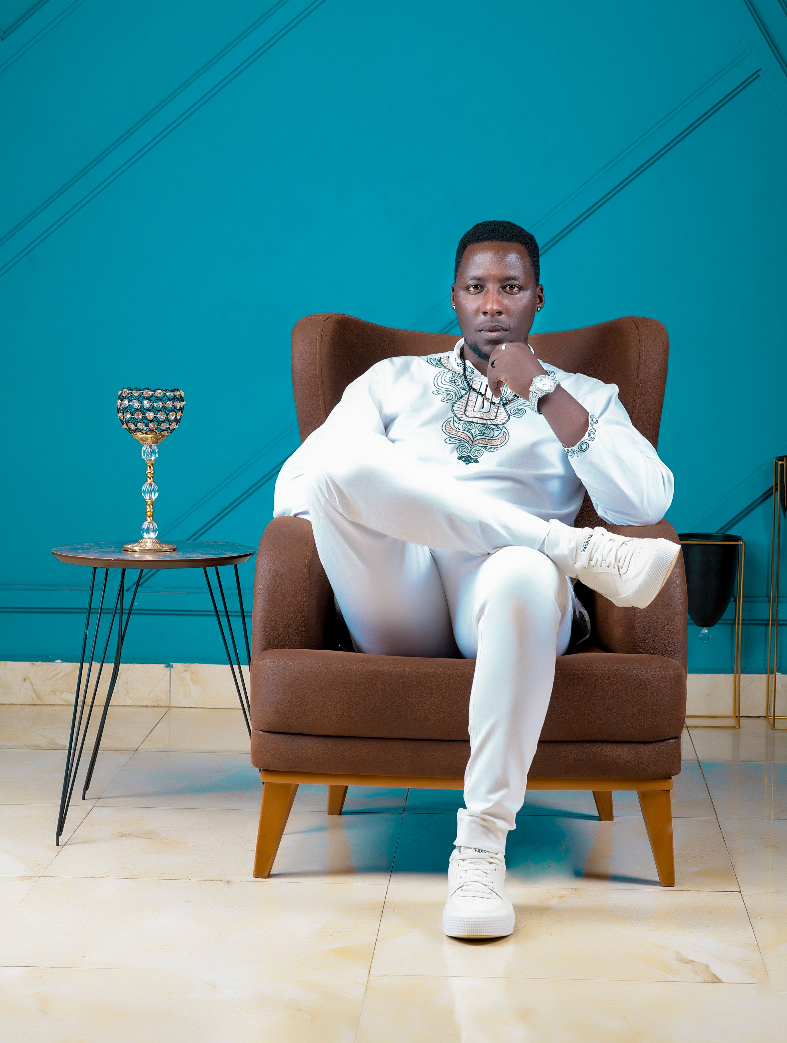 Man elegantly dressed in white sitting on armchair in stylish room with blue wall.
