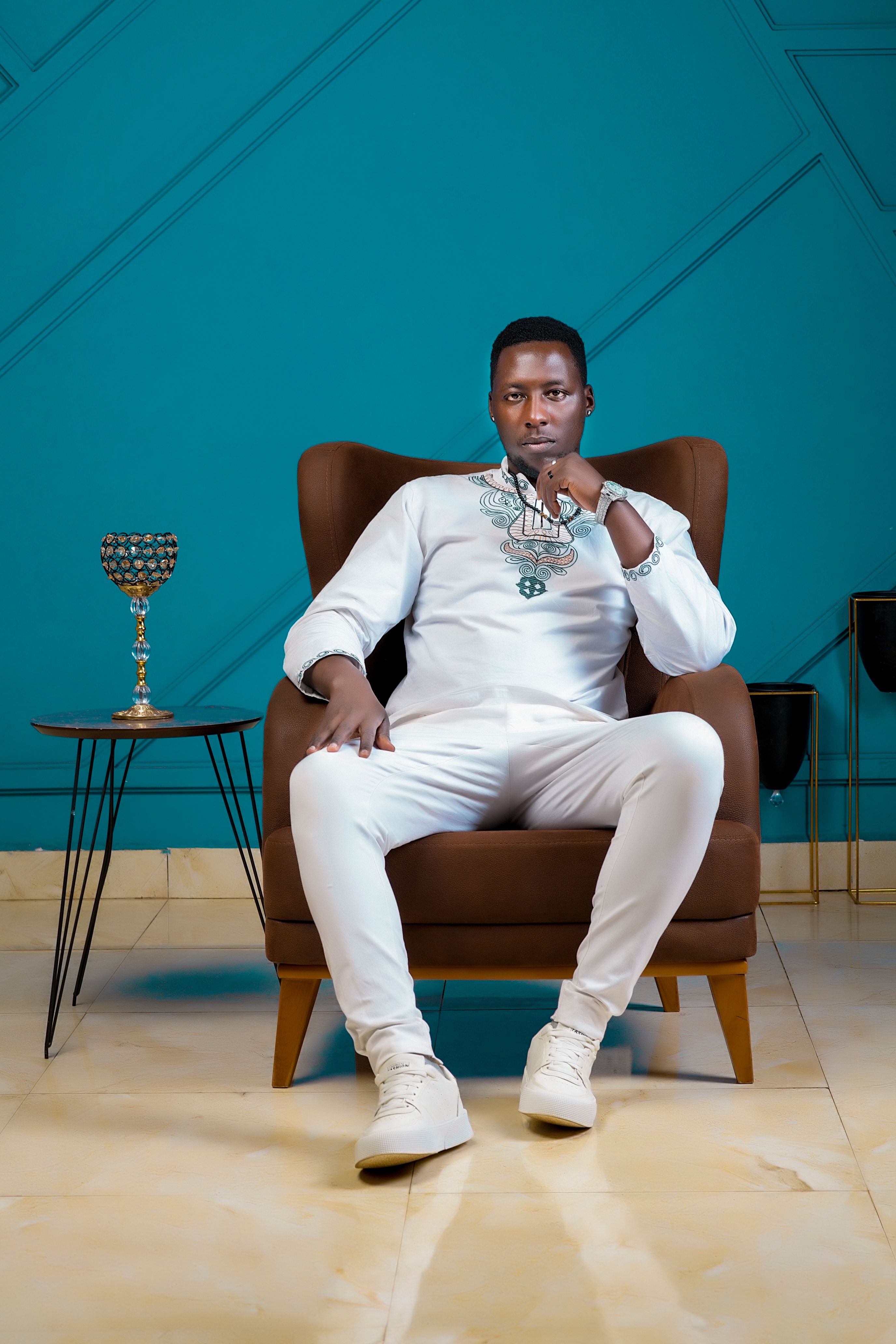 Portrait of a fashionable man in white attire seated in a stylish armchair.