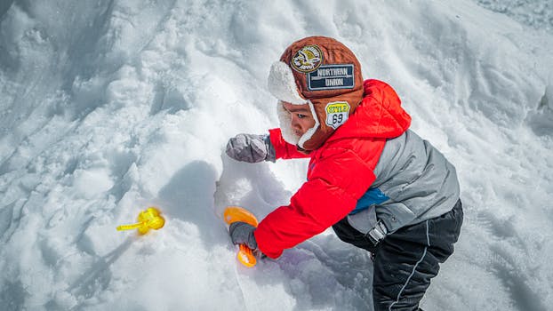 A child wearing a warm jacket and hat playing in the snow on a bright winter day.