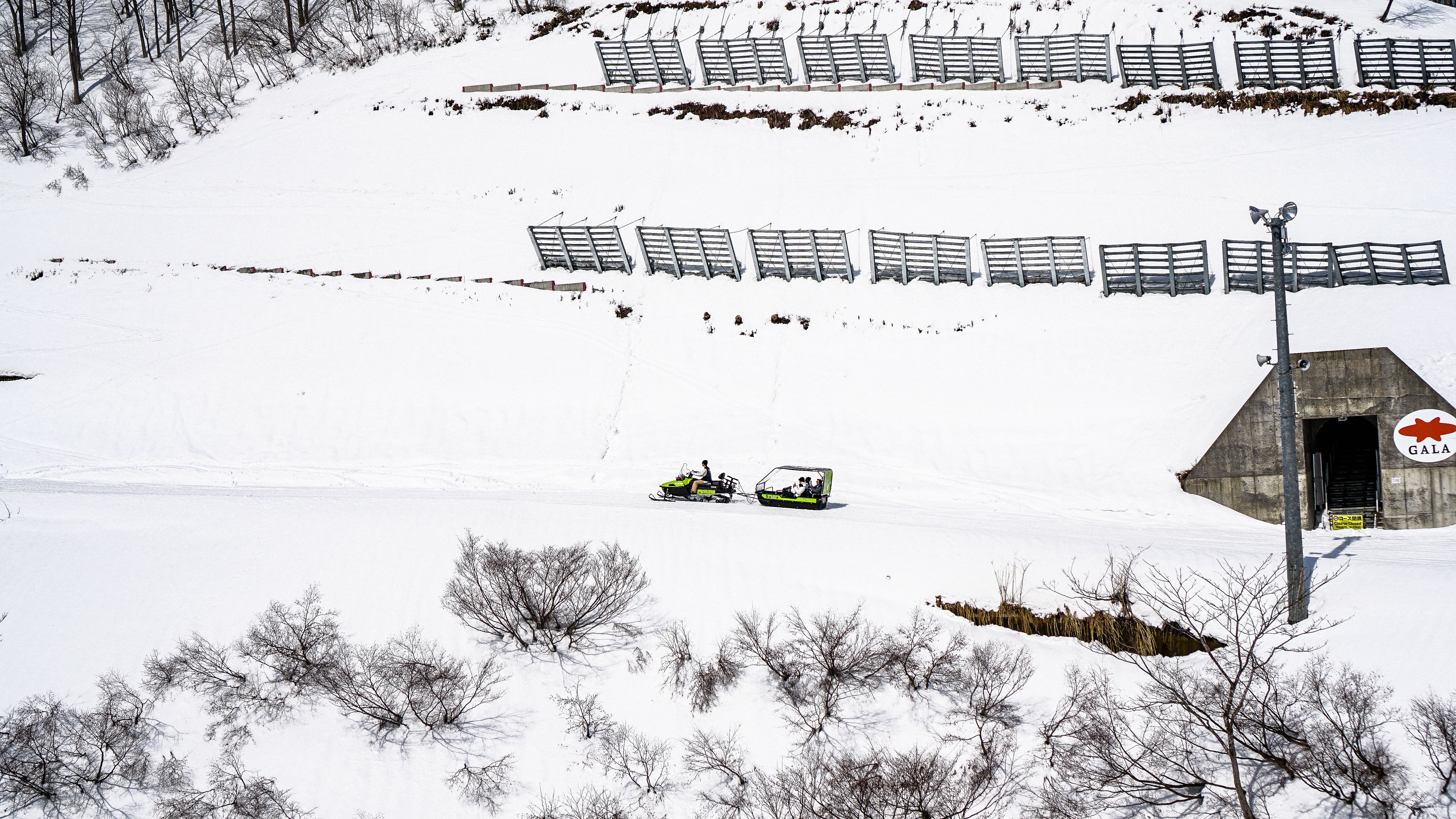Aerial view of snow-covered landscape with snowmobiles near a bunker entrance in winter.