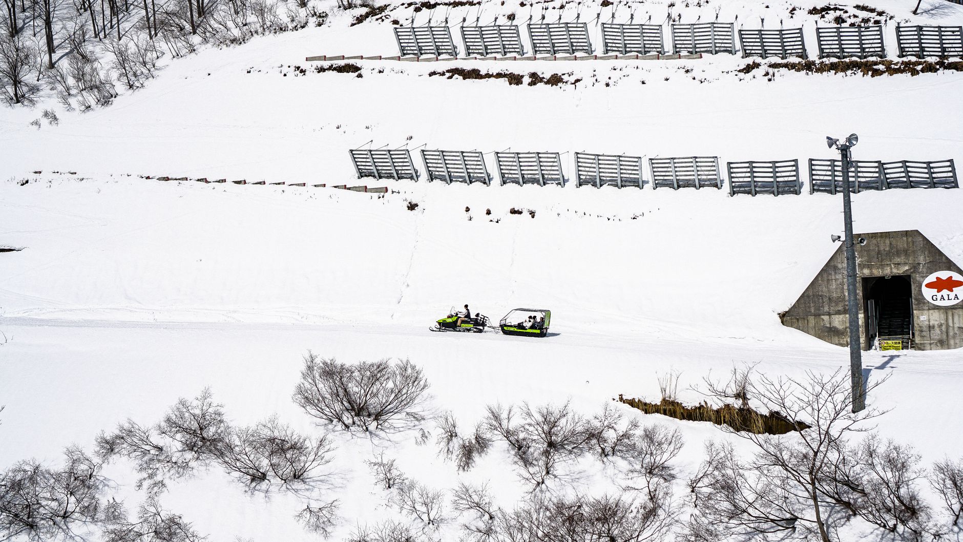 Aerial view of snow-covered landscape with snowmobiles near a bunker entrance in winter.