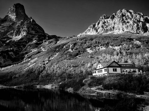 Free Black and white image of a house by a serene lake with mountains. Stock Photo