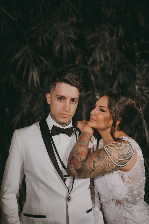 A bride and groom in white suits and tattoos