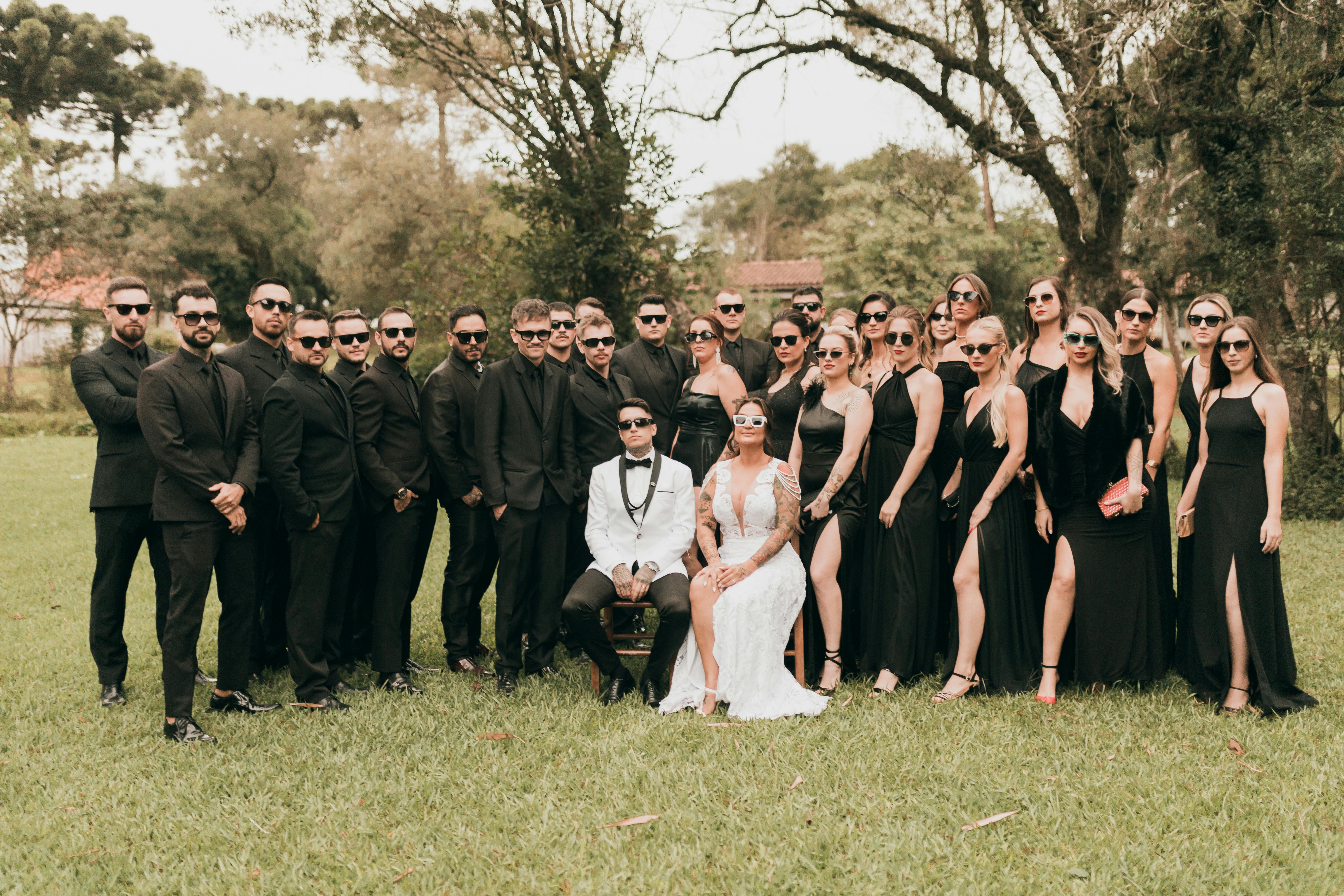 A chic wedding party gathering outdoors with guests in black attire and newlyweds in white.