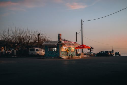 Free Serene dusk view of a seaside kiosk with colorful umbrella and parked cars under a calm twilight sky. Stock Photo