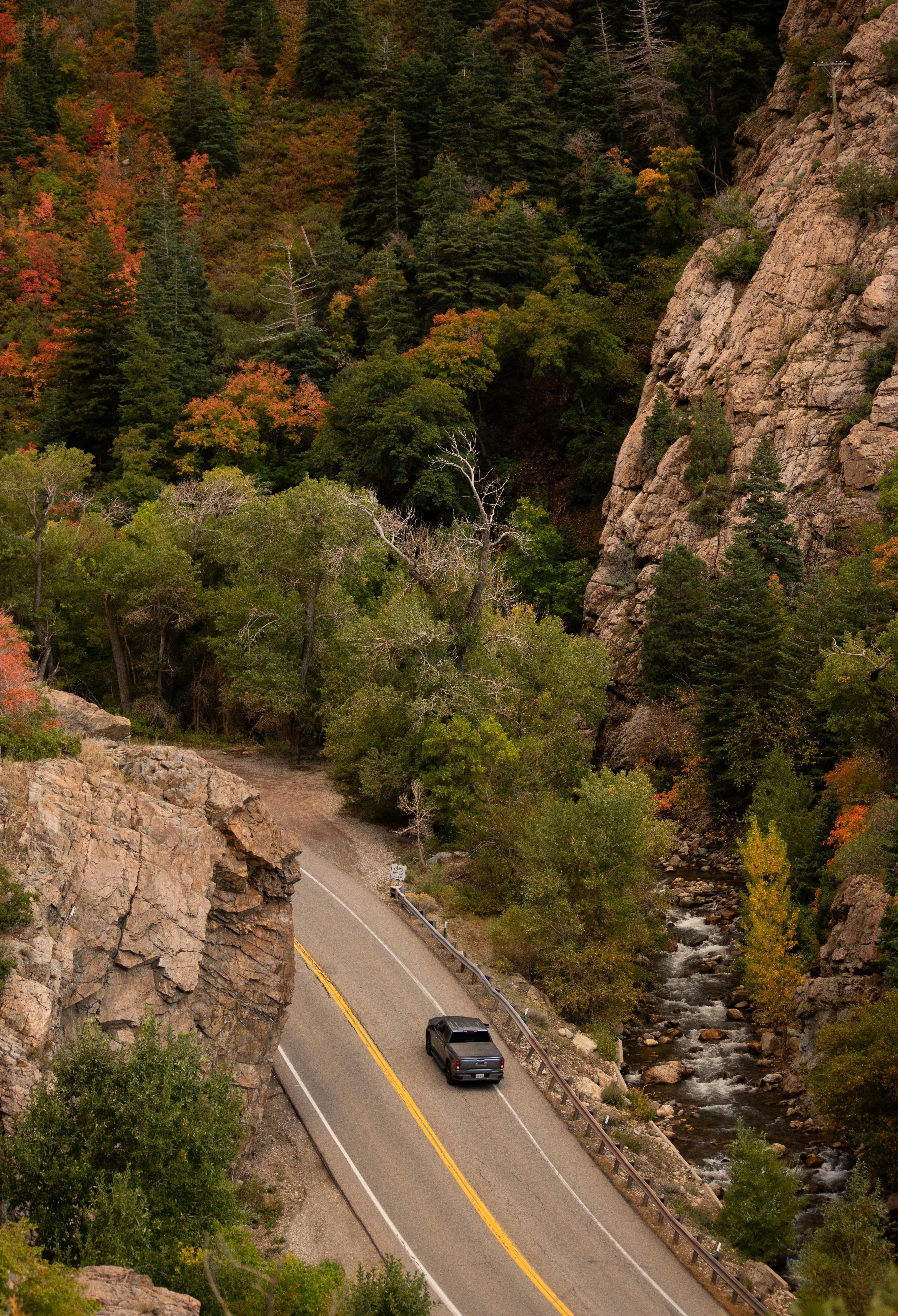 Aerial view of a car driving through a picturesque canyon with vibrant fall foliage.