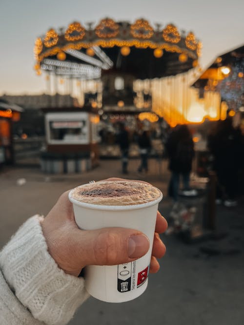 A person holding a cup of coffee in front of a carousel