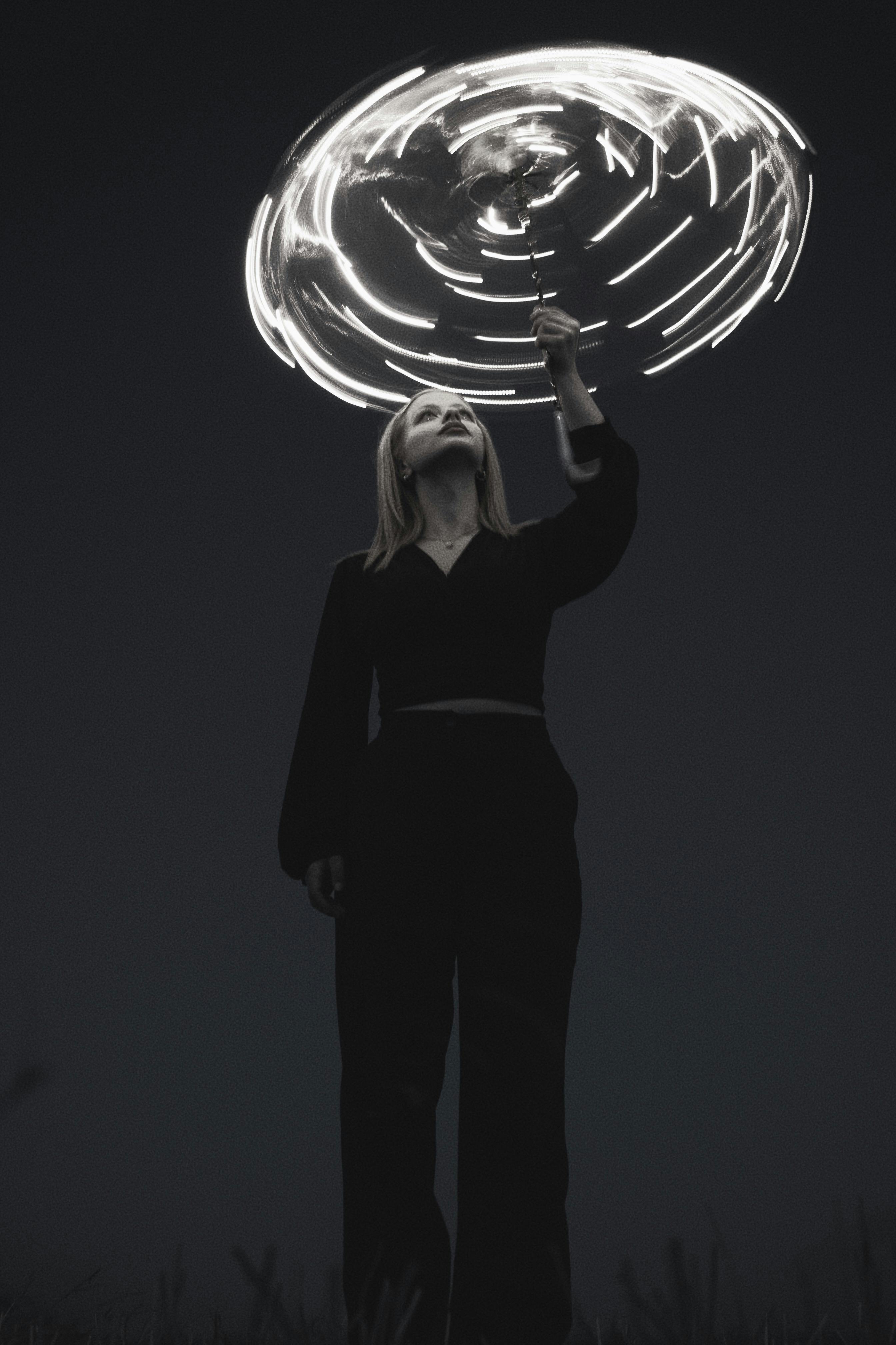 A young woman holding a light-painted umbrella at night, creating glowing spiral trails.