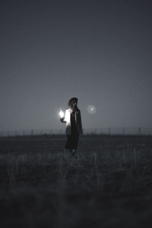 Free A silhouette of a woman holding a glowing lamp in a dark empty field, creating an eerie vibe. Stock Photo