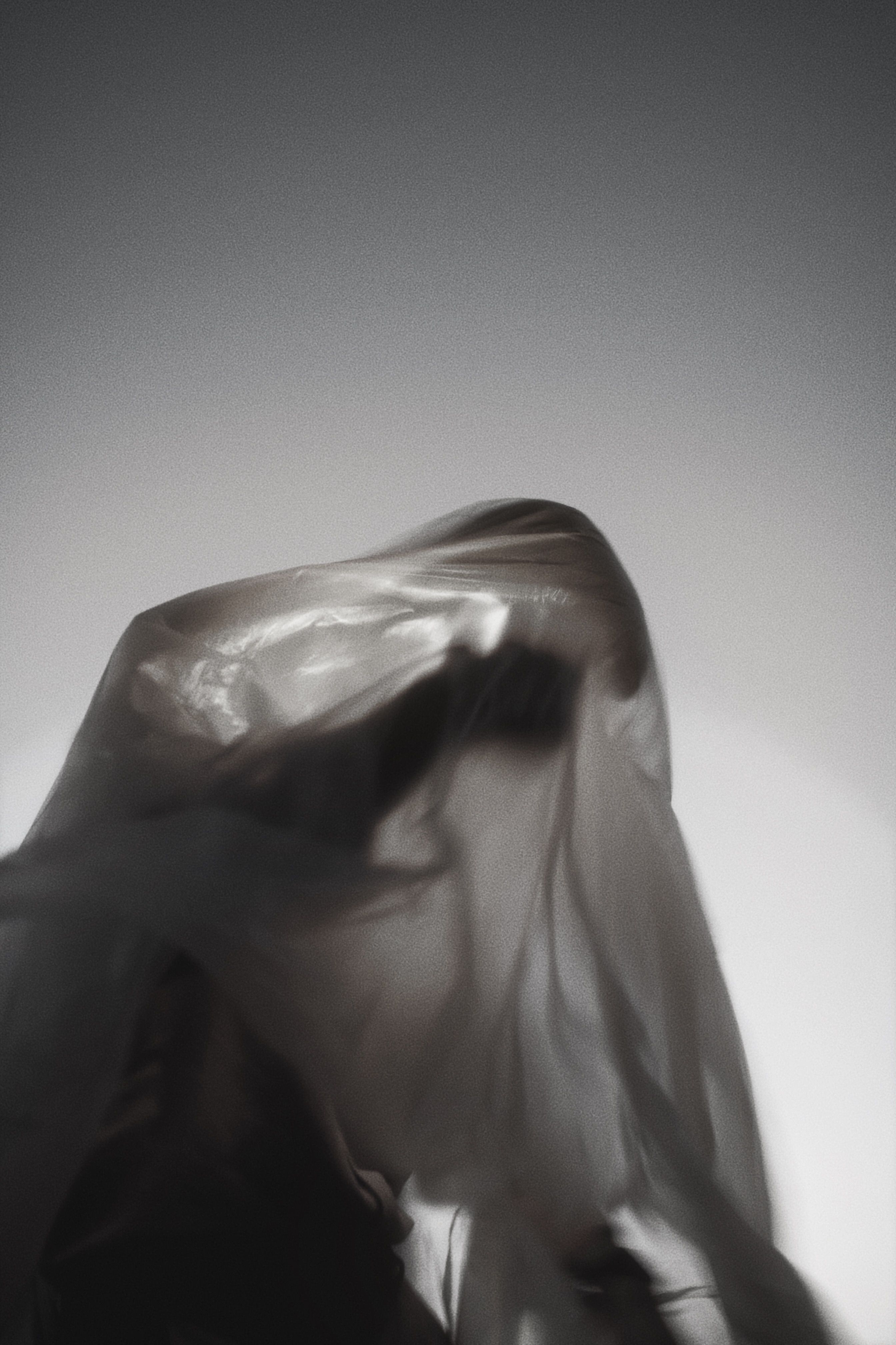 Artistic black and white silhouette of a figure draped in translucent fabric, evoking mystery.