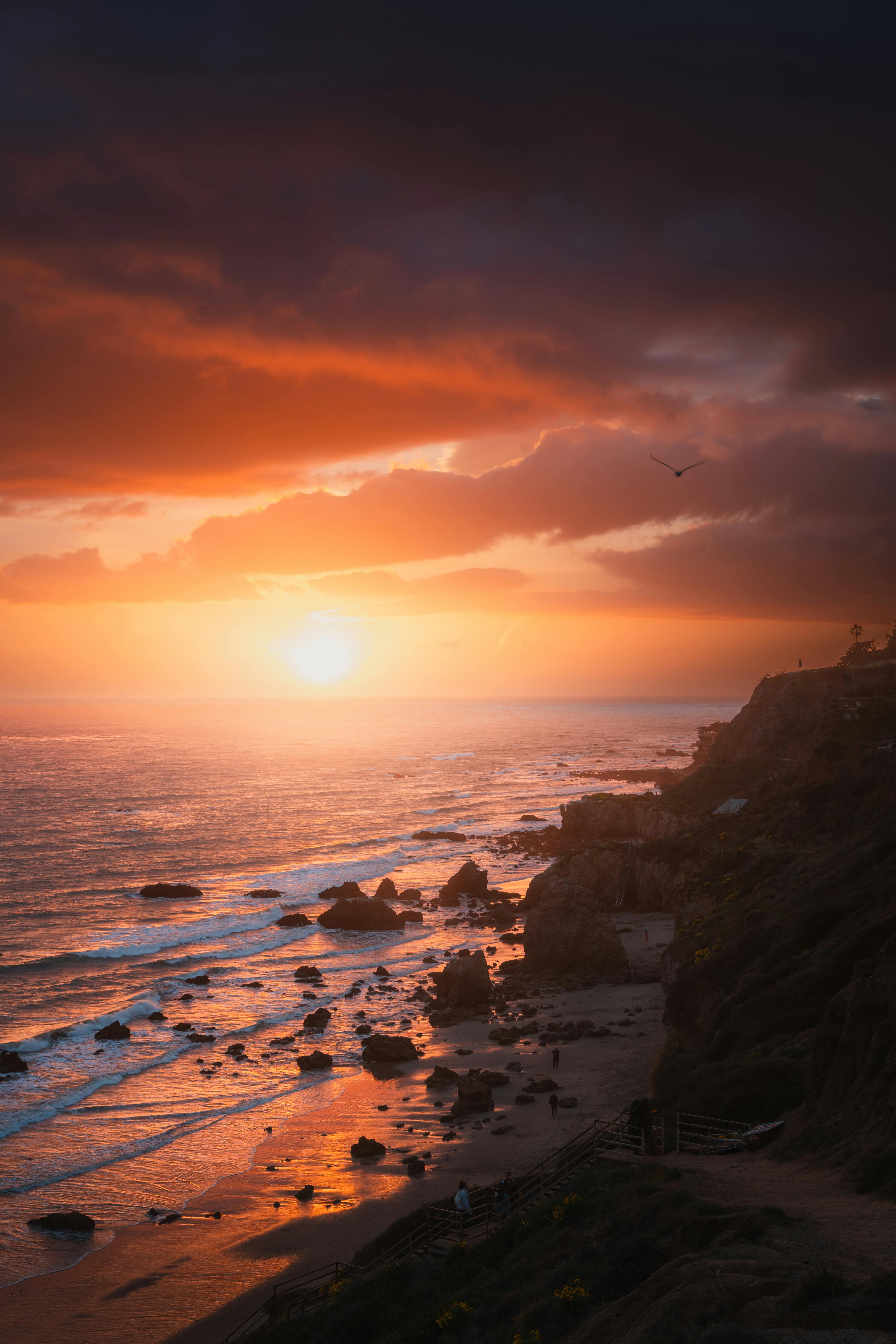 Stunning sunset over Malibu's rocky shoreline with vibrant skies and ocean waves.