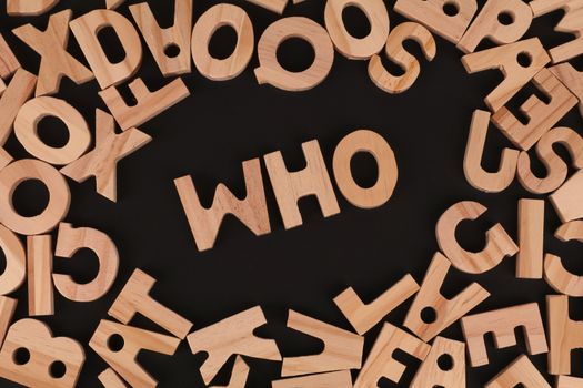 Wooden alphabet letters arranged to spell 'Who' on a black surface, creative message concept.