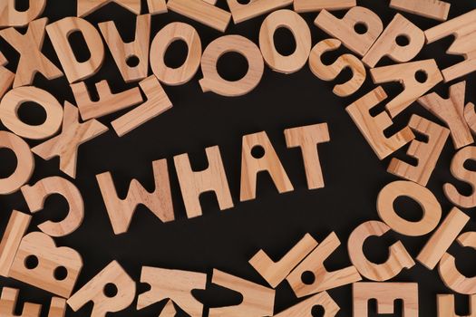 Artistic arrangement of wooden letters spelling 'WHAT' on a black background, offering creative inspiration.
