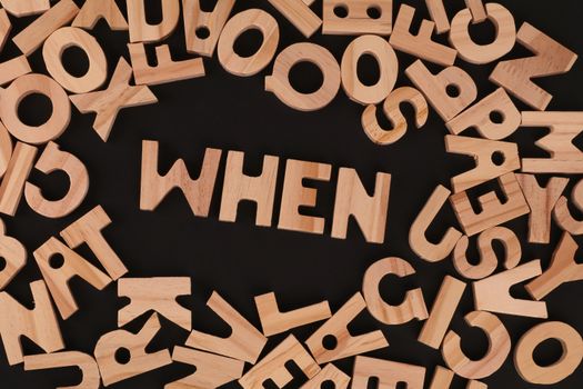 Scattered wooden alphabet letters with the word 'WHEN' on a black surface, creative concept.