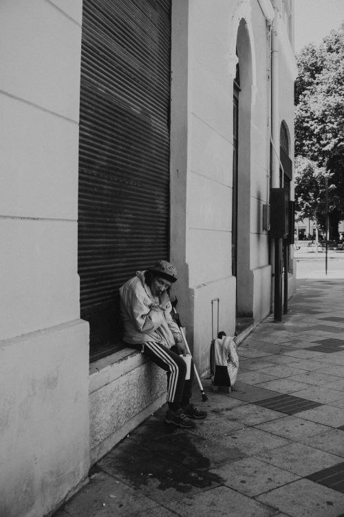 Free Monochrome image of an elderly woman resting on a city sidewalk in Valdivia, Chile. Stock Photo