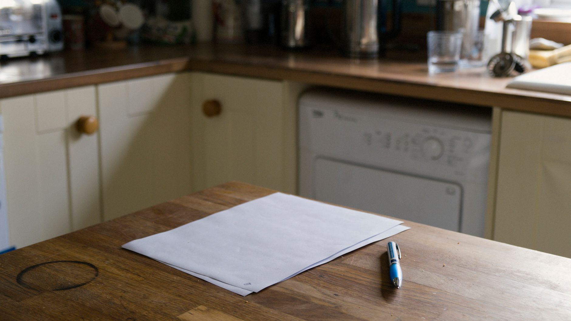 A blank sheet of paper and a pen on a wooden kitchen table, ready for the gift letter behind gift money for a down payment