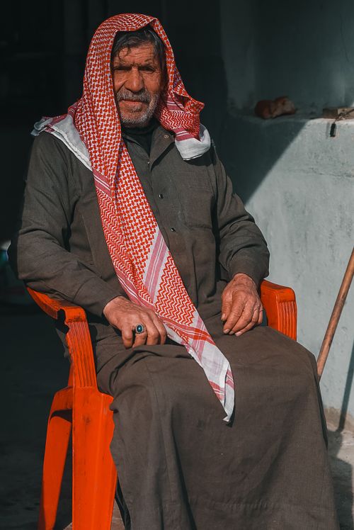 Free Senior adult man with a mustache wearing a headscarf, seated outdoors in a plastic chair. Stock Photo