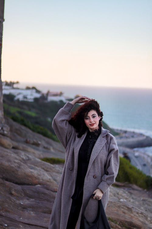 A woman in a coat standing on a cliff overlooking the ocean