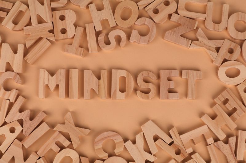 Những chữ cái gỗ xếp thành từ ‘Mindset’ trên nền pastel, tượng trưng cho tư duy và cách nhìn nhận bản thân