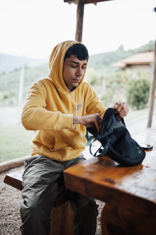 A young man in a yellow hoodie is sitting at a table