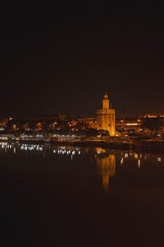 Illuminated Torre del Oro reflected in the Guadalquivir River at night in Seville, Spain.