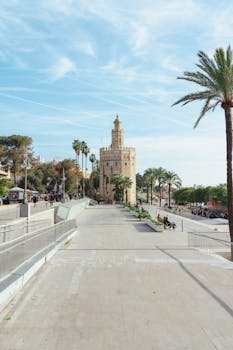Majestic Torre del Oro tower in Seville, Spain, surrounded by palm trees under a bright blue sky.