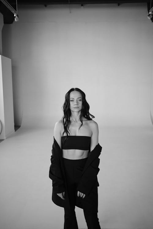 A woman in a black crop top and pants standing in a studio