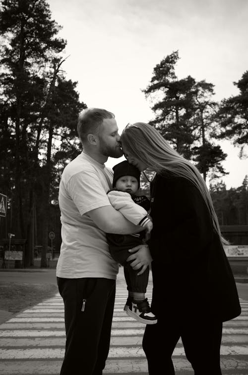 A man and woman kiss their baby in black and white