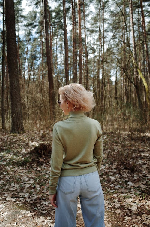 A woman in a green sweater stands in the woods