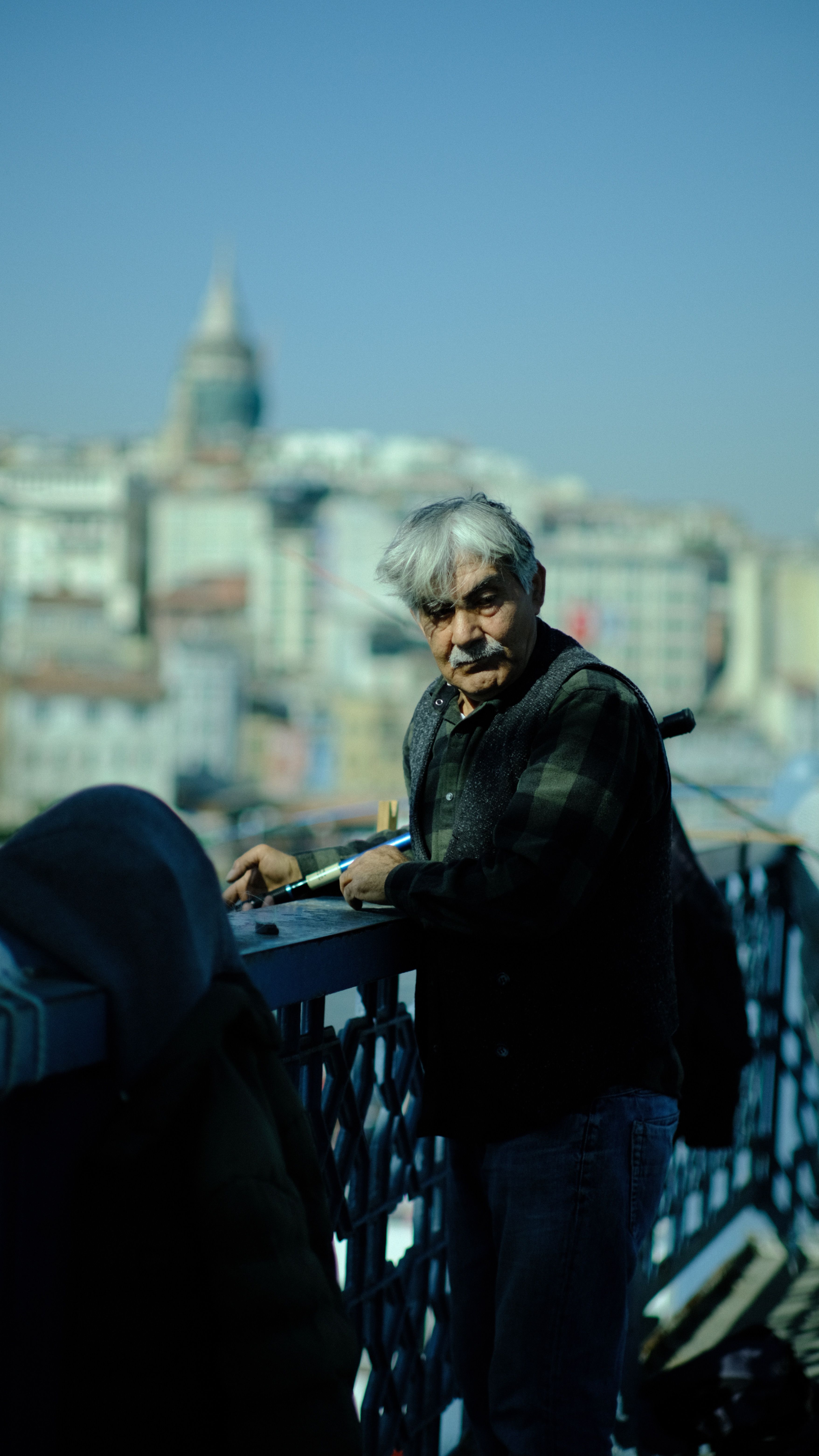 Istanbul fisherman on Galata Bridge, city skyline in background, capturing urban life.