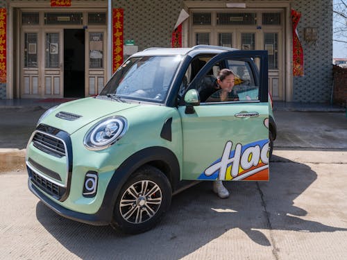 A small green mini car with a man standing next to it