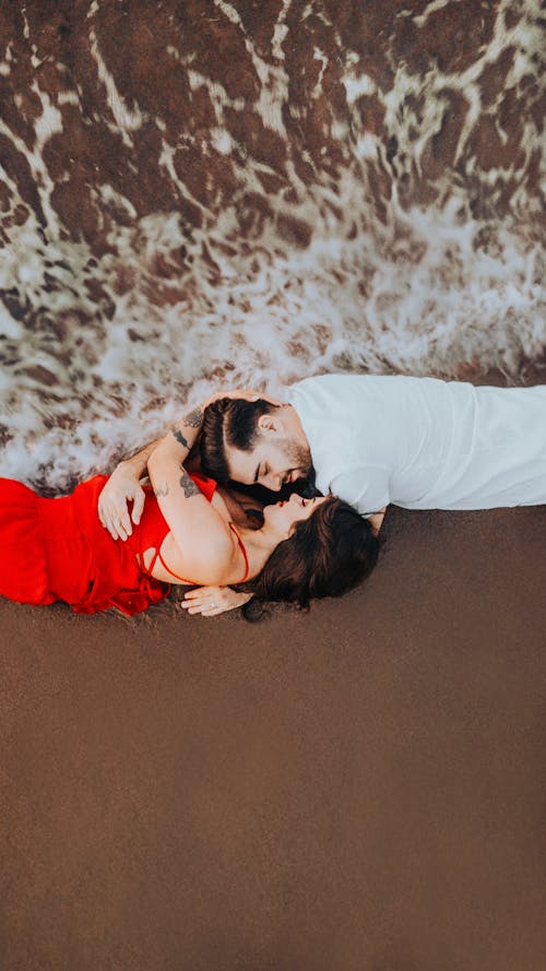 A couple laying on the beach in red dress