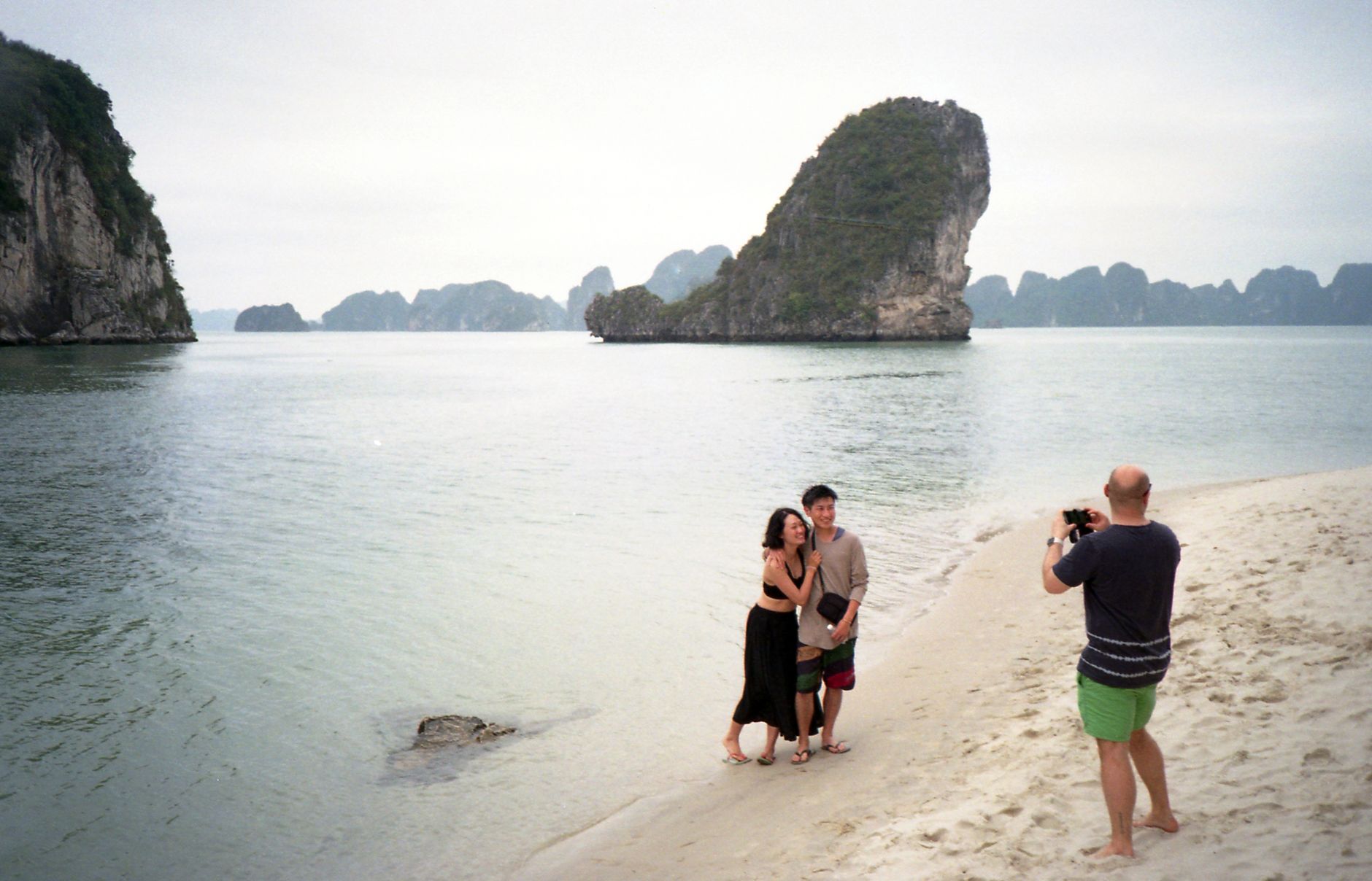 A couple posing on a scenic beach in Ha Long Bay, Vietnam, captured during daytime.