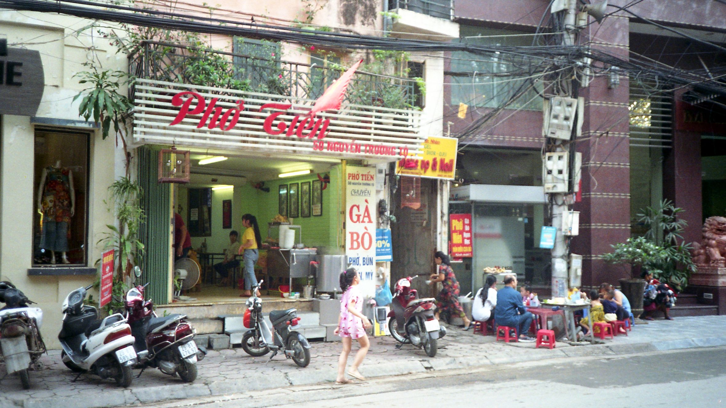 An outdoor scene of a bustling Vietnamese restaurant with people dining on the sidewalk in Hanoi.