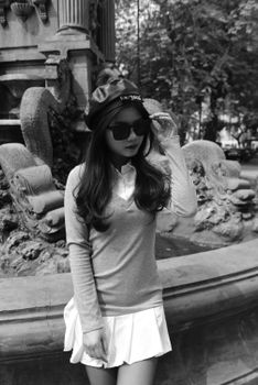 Black and white photo of woman in fashionable outfit by a fountain.