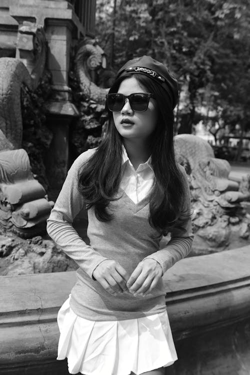 A woman in sunglasses and a skirt posing in front of a fountain