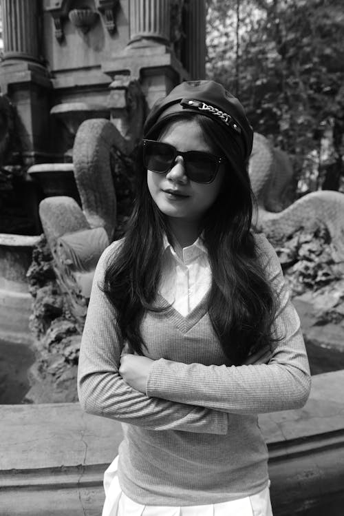 A woman in sunglasses and a hat posing in front of a fountain